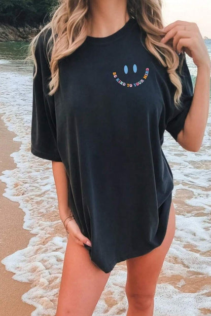 Front view of an oversized black t-shirt with a top left chest design of two blue eyes and the words 'Be Kind To Your Mind' forming the shape of the mouth to make a smiley face.;