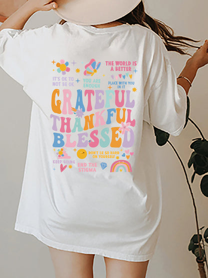 Back view of an oversized white t-shirt with colourful text and graphics reading 'Grateful Thankful Blessed' surrounded by inspirational phrases such as 'You Are Enough', 'It's Ok to Not Be Ok' and 'End the Stigma', along with cheerful design of flowers, butterflies, heats and rainbows.