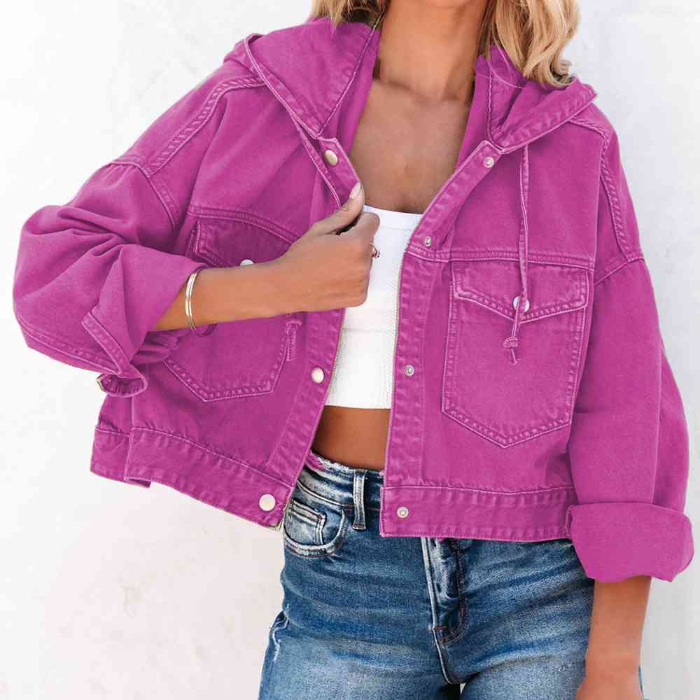 A stylish fuchsia oversized hooded denim jacket with a button up front, flap pockets and adjustable drawstring hood. The Jacket features a relaxed fit with rolled-up sleeves, paired with a white crop top and blue jeans for a casual trendy look.